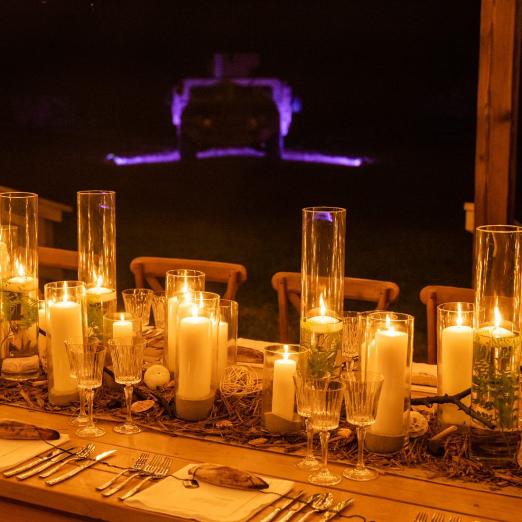 Candles in multi sized pillar vases on a wooden dining table.