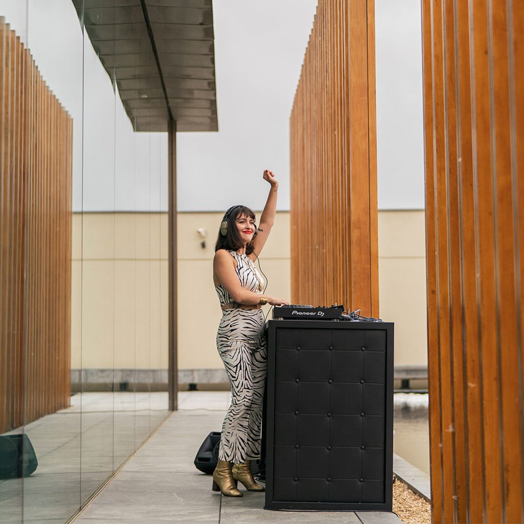 Woman with raised arm in silver dress standing in front of a black DJ booth