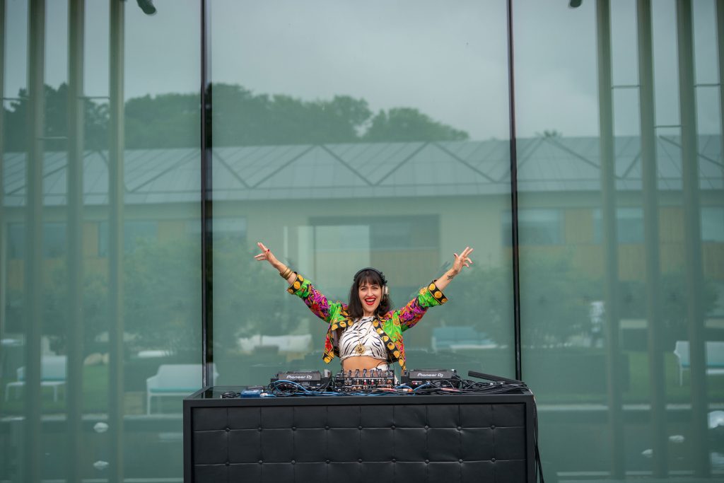 A woman with her arms up in a v shape at DJ decks. Luxury Party Planners.