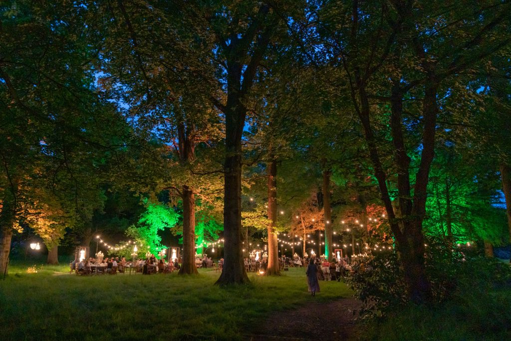 A woodlands with many dining tables arranged within a central area with atmospheric lighting. Luxury Private Event Planner.