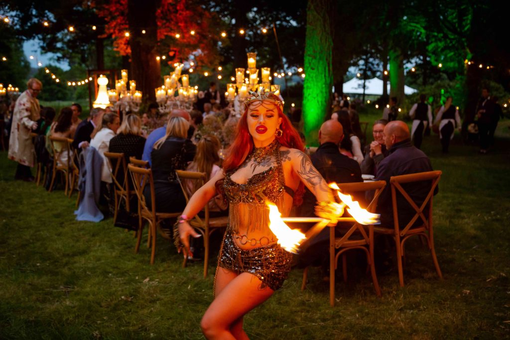A fire performer entertaining guests at a dinner party on a lawn under fairy lights