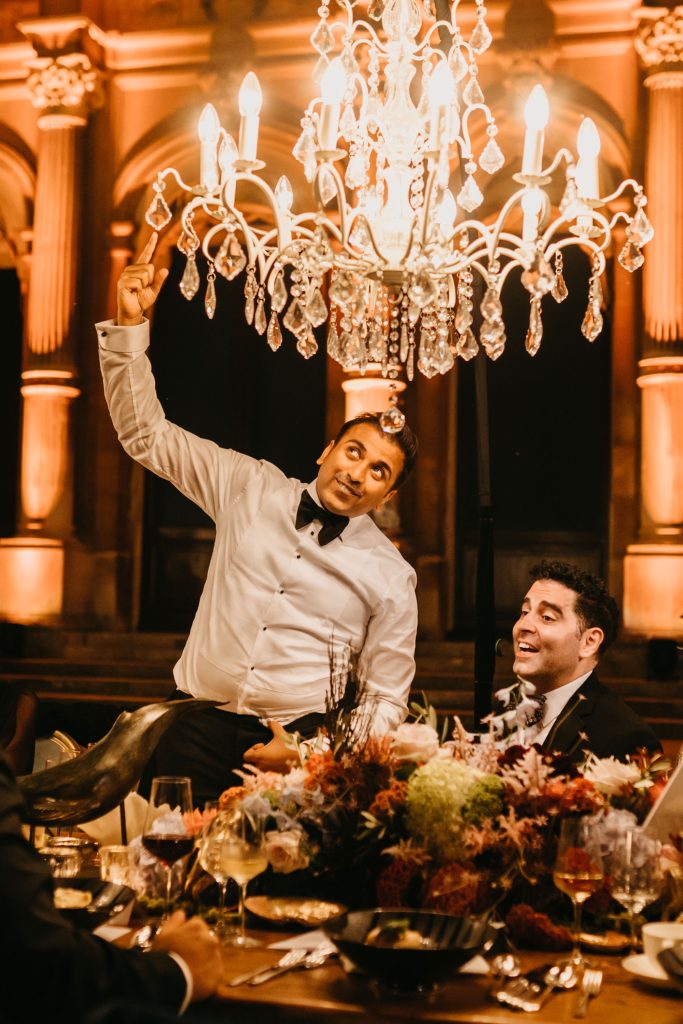 A man in a white shirt and black bowtie reaching up to a white chandelier