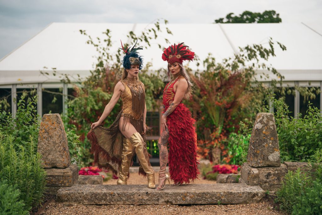 Two mythically dressed character performers stood in front of a white marquee and floral installation.