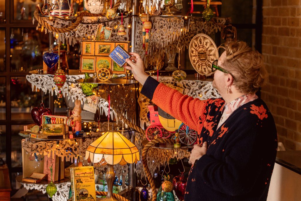 A man placing a tin on a metal tree structure that is laden with other antique props. Christmas party planners.