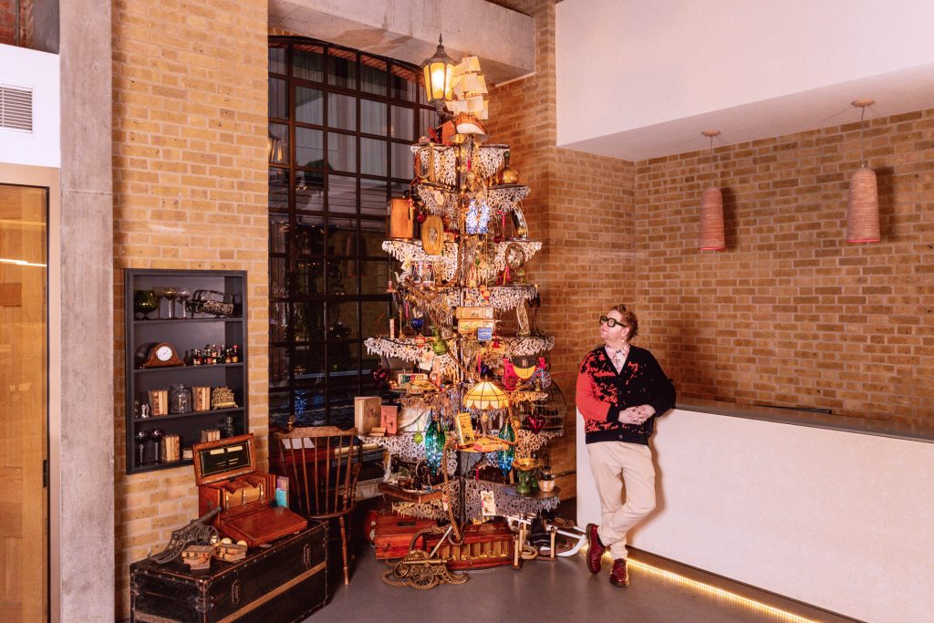 A man gazing up at a Christmas Tree made of metal dressed heavily in Victorian and antique objects