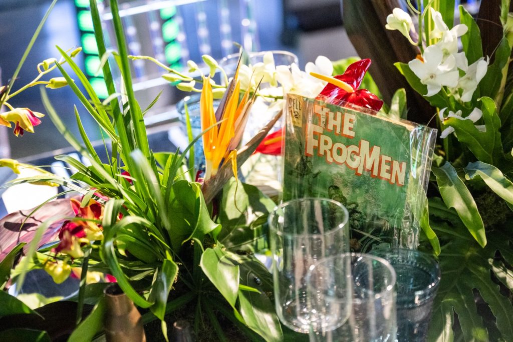 A 'Frogman' comic amongst exotic flowers and glassware.