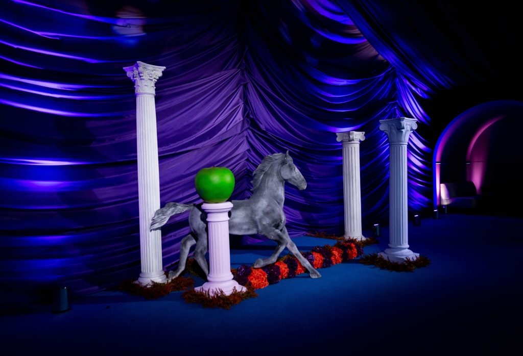 Theatrical props including pillars, a large green apple and a silver horse.