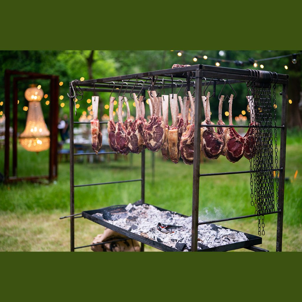 Tomahawk steaks cooking over charcoal on a large frame