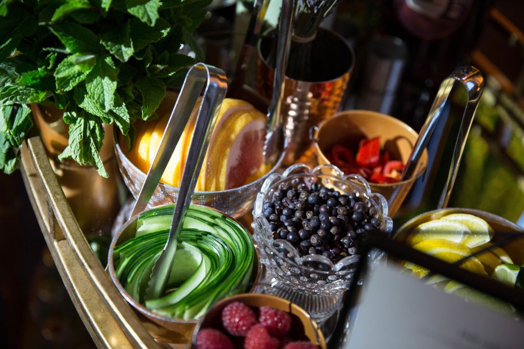 Garnishes for cocktails including cucumber ribbons, blueberries, lemon wedges and basil