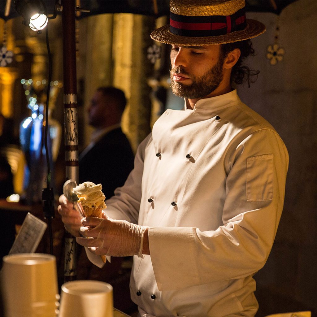 Man wearing a white uniform and straw hat serving ice cream.