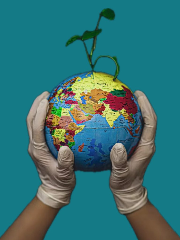 A pair of hands wearing white gloves holding a globe with a green plant shoot sprouting out the top.