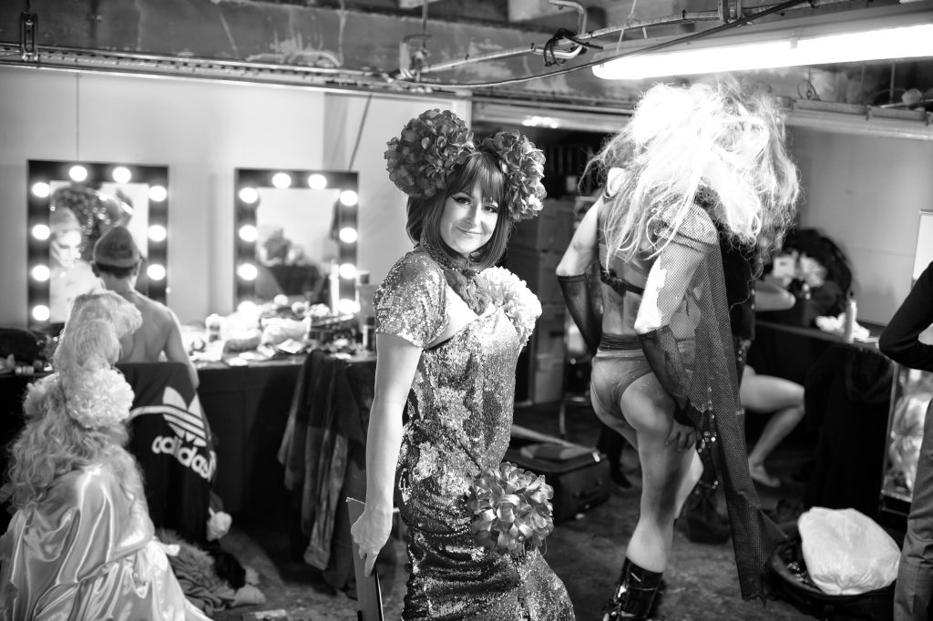 Monochrome photo of character performers in costume and drag in front of theatrical mirrors.