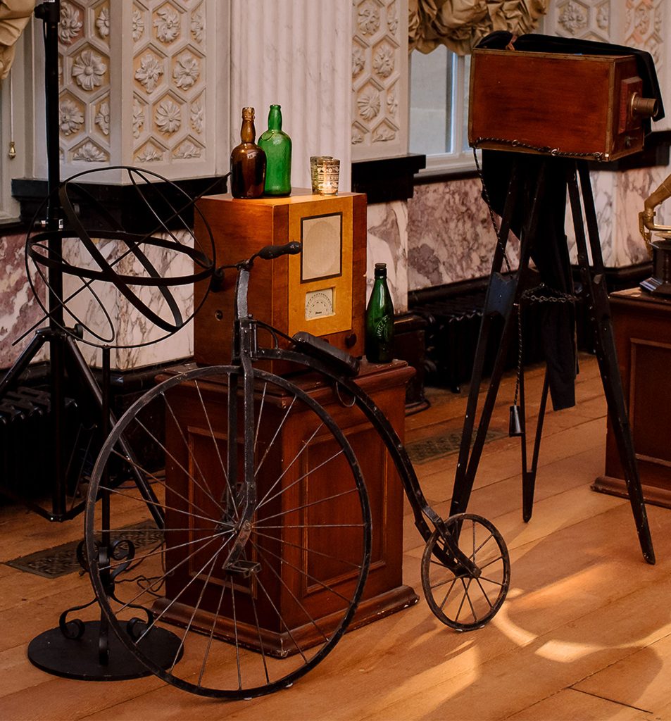 A variety of antiques including a penny farthing, a wireless radio and an old projector.