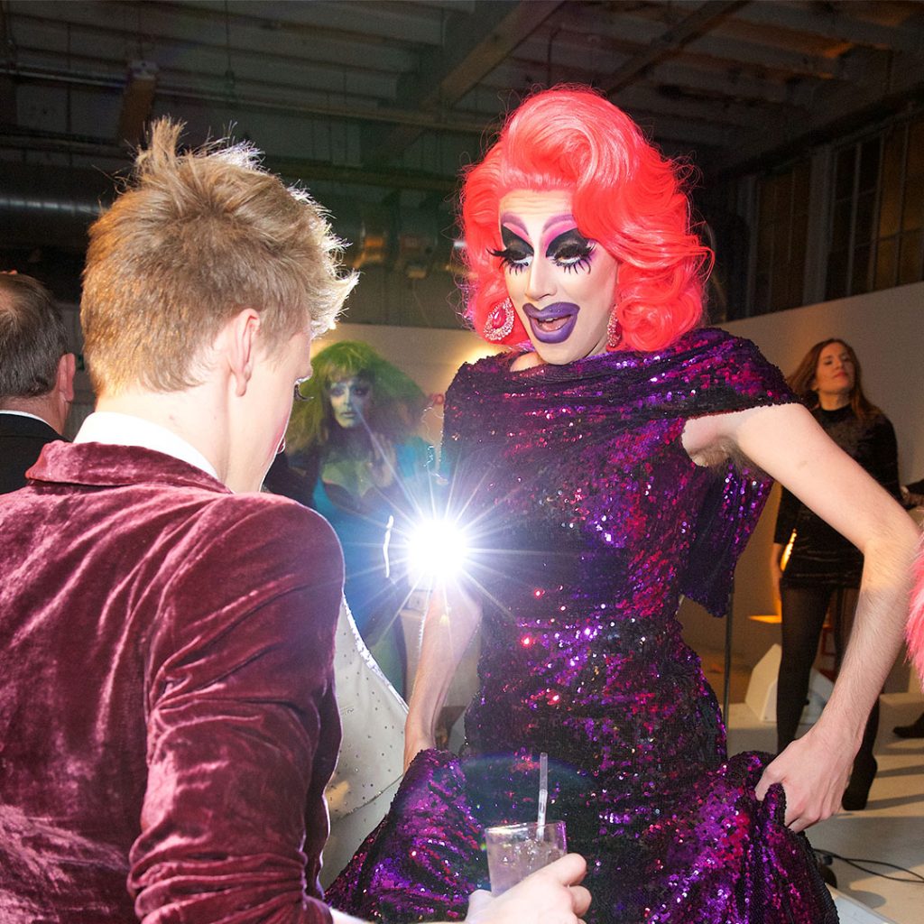A drag queen with a red wig and purple shimmering dress